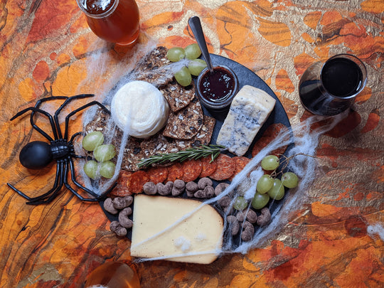 Halloween themed cheese board with beer and charcuterie pairings, fake spiderwebs, and fake spiders