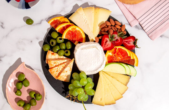 circular slate serving board styled with cheese, fruit, and olives on marble table