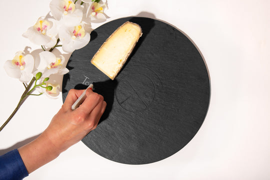 circular slate serving board with cheese, flowers, and hand labeling with soapstone chalk